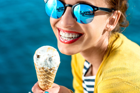 ice cream: Phụ nữ trẻ trong chiếc áo len màu vàng và kính mát ăn kem trên nền nước xanh Kho ảnh