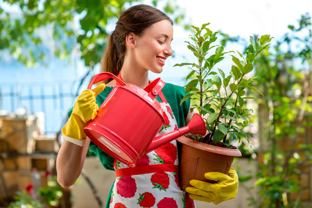 Young woman in apron and working gloves taking care for flower in in the garden