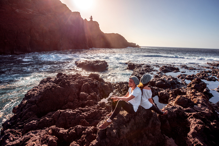 若いカップルは白い上に座って一緒に岩の海の海岸に夕日に身を包んだ コピー スペースを持つ広角イメージ の写真素材 画像素材 Image