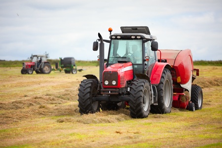 huge tractor collecting haystack in the field in a nice blue stock