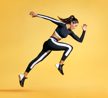 Sporty woman runner in silhouette on yellow background. Photo of attractive woman in fashionable sportswear. Dynamic movement. Side view. Sport and healthy lifestyle Stockfoto - 103368270
