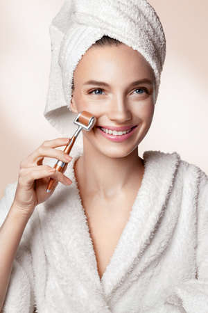 Belle femme utilisant un rouleau de derma pour sa peau du visage. photo de femme avec une peau parfaite sur fond beige. concept de beauté et de soins de la peau Banque d'images