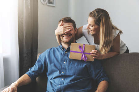 Femme donnant un cadeau surprise à un homme bien-aimé à la maison. yeux fermés avec la main par derrière