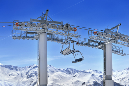 Empty chair lift above snowy mountain and under blue sky