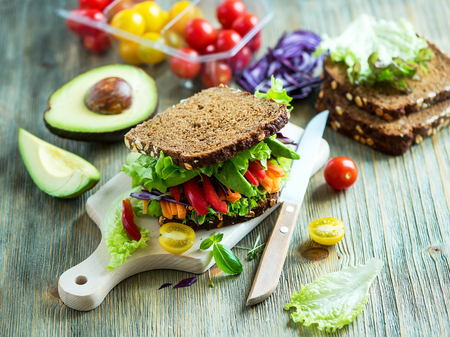 Sandwich au seigle végétalien avec des ingrédients frais: avocat, salade, tomate, carottes, pour des repas sains, des vitamines et des aliments diététiques