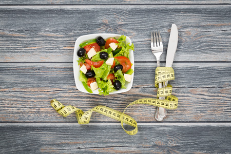 Salade de remise en forme et ruban à mesurer sur une table en bois rustique.