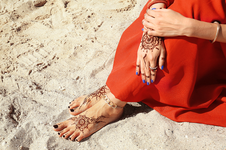 Female legs and hands with henna tattoo on beach sand background - 107689859