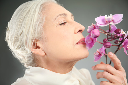 Beautiful Elegant Elderly Woman With Orchid Flowers On Gray Background