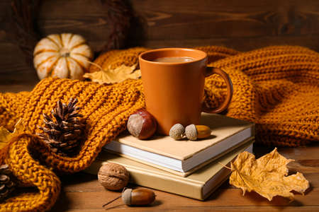 Cup of tasty coffee, books and autumn decor on wooden background