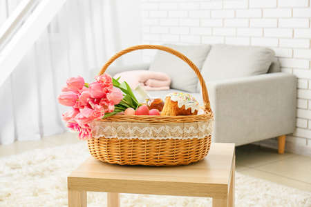 Panier-cadeau avec des oeufs de pâques peints, des fleurs de tulipe, une bouteille de vin et un gâteau sur la table dans la chambre Banque d'images