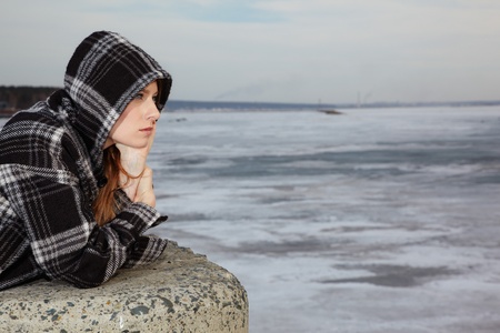 sad lonely: Blonde girl near winter river covered by ice