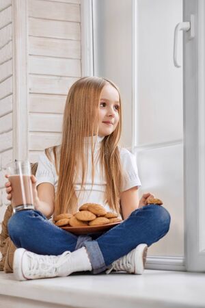 かわいい女の子はクッキープレートと窓枠に座っています の写真素材 画像素材 Image