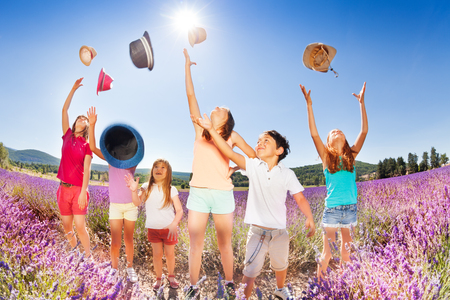 Happy kids tossing up hats over blue sky in summer