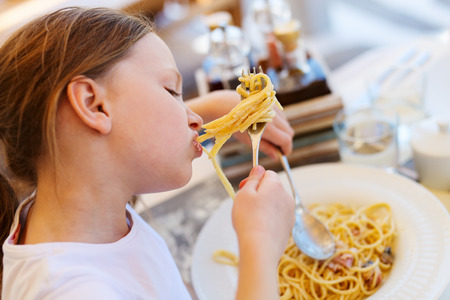 Porträt des entzückenden kleinen Mädchens, das Spaghettis für ein Mittagessen am Restaurant isst