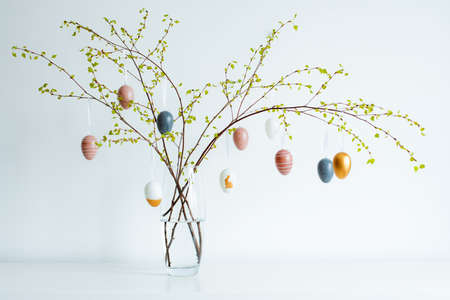 Vase avec des branches printanières d'arbres en fleurs, des oeufs de pâques colorés sur un tableau blanc Banque d'images
