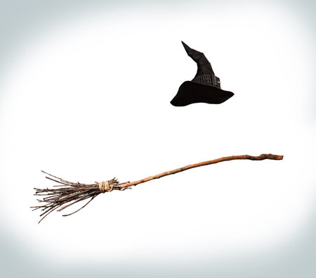 Classic pointed witch hat and flying broom flying on a white background Фото со стока