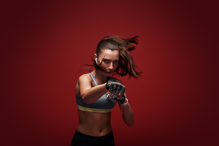 Hustle to gain more muscle. sportswoman standing concentrated in gym gloves over red background.