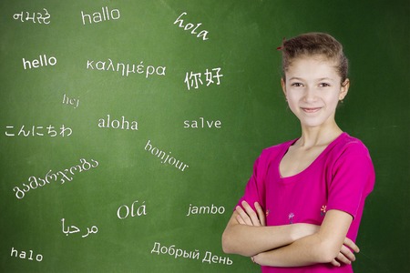 Learning foreign languages. Portrait confident teenager girl student standing by chalkboard with word hello written in different foreign languages. Education concept, international communication