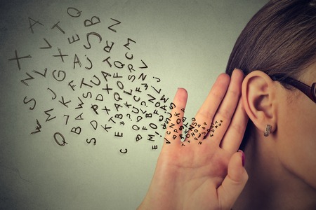 Woman holds her hand near ear and listens carefully alphabet letters flying in isolated on gray wall background  - 59998668