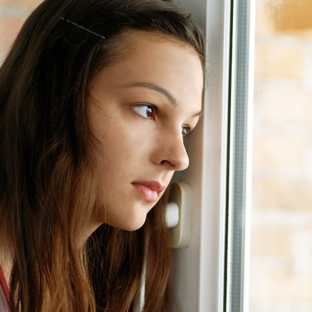 sad lonely: caucasian teenage girl portrait looking out window