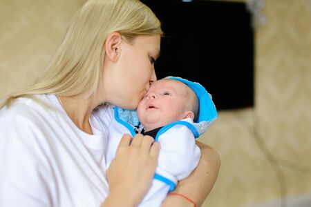 若い母親は 赤ちゃんに話す子 そっと手をつないで歌をなだめるような歌の世話します おむつの赤ちゃんは眉をひそめるし 泣く 母親の手を繋いで 光の部屋で手で中腰を横になっています 白 T に身を包んだ女性金髪欧州外観 の写真素材 画像素材 Image