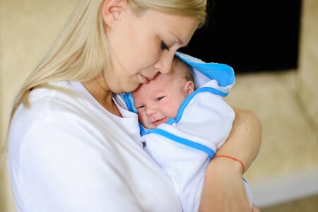 若い母親は 赤ちゃんに話す子 そっと手をつないで歌をなだめるような歌の世話します おむつの赤ちゃんは眉をひそめるし 泣く 母親の手を繋いで 光の部屋で手で中腰を横になっています 白 T に身を包んだ女性金髪欧州外観 の写真素材 画像素材 Image