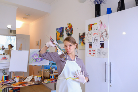 かわいい女性画家と壁の白い絵画スタジオに立って手でブラシとカラフル パレット笑顔 ポーズ 笑うとカメラの前で浮気します 女の子欧州外観大人と子供のための美術学校を宣伝します の写真素材 画像素材 Image