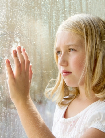 sad lonely: Teen or child looking out a window with rain