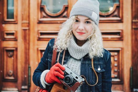 レトロなフィルム カメラ雪冬市の背景に写真を撮影で暖かい服装で若い金髪巻き毛笑みを浮かべて女性 の写真素材 画像素材 Image