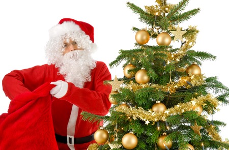 Santa Claus Beside A Christmas Tree With Gold Ornaments Looking Into The Camera And Reaching Santa Claus Beside A Christmas Tree With Gold Ornaments Looking Into The Camera And Reaching
