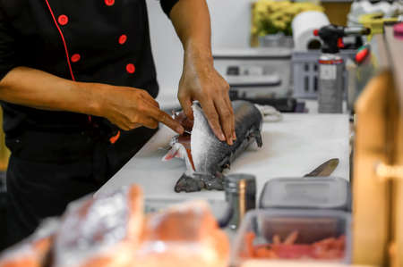 Filete de salmón fresco en la mesa de la tabla de cortar blanca mientras el chef filetea o rebana en la sala de cocina. selección de enfoque en la mano mientras se corta con disparo de enfoque suave.