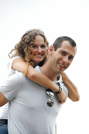 beautiful curly haired smiling woman with arms wrapped around the shoulders of happy handsome man both looking towards viewer. shot on overcast day providing soft lighting and making the sky appear whitish