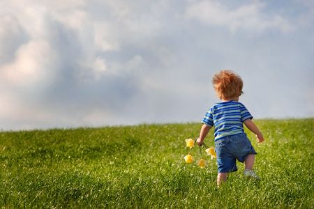 Young boy walks up a hill while holding a handfull of flowers. There are storm clouds in the sky.