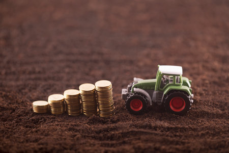 Tractor miniature with coins on fertile soil land Reklamní fotografie
