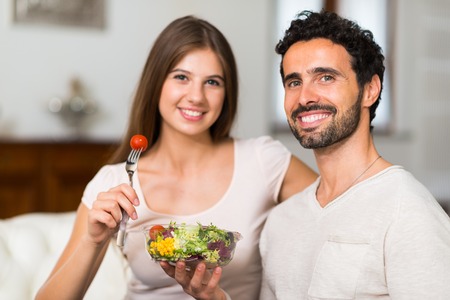 Couple eating a salad in the living room Imagens