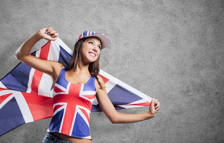 Cheerful cute English girl holding a flag, wearing a tank top and a cap with Union Jack flag, patriotism and enjoyment concept Stock Photo