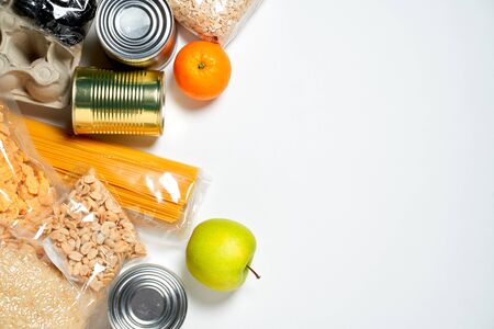 Różne produkty spożywcze zamknięte w plastikowych torebkach, puszkach i owocach na białym tle, widok z góry. Zdjęcie Seryjne