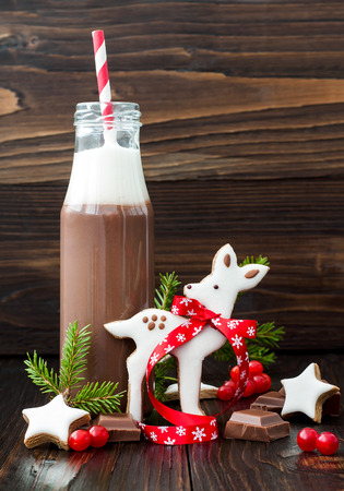 Hot chocolate with whipped cream in old-fashioned retro bottles with red striped straws. Christmas holiday drink and gingerbread baby deer or fawn cookies. Free text copy space