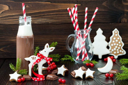 Hot chocolate with whipped cream in old-fashioned retro bottles with red striped straws. Christmas holiday drink and gingerbread baby deer or fawn cookies