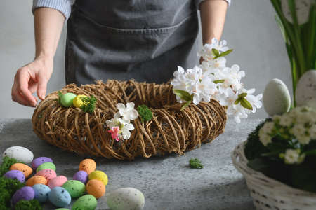 Femme faisant une couronne florale de pâques de matériaux naturels de fleurs et d'œufs.