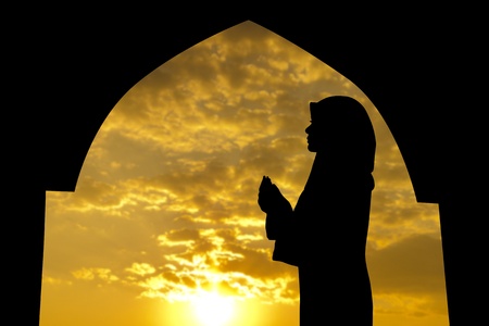 personas orando: Silueta de Mujer musulmana rezando en la mezquita durante el tiempo de puesta de sol Foto de archivo