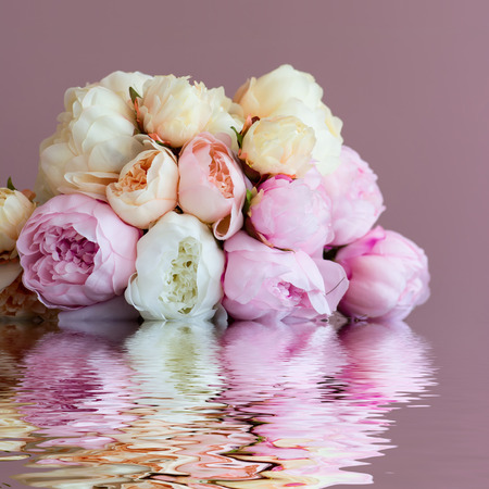 Peach flower: Bouquet made of artifical pink peony laying on a watersurface. Shot against pink wall background. Shallow DOF.