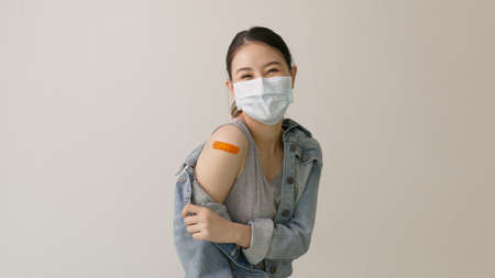 Young attractive beautiful asia female or teenage receive covid-19 anti virus vaccine in campaign vaccination safe life happy smile cheerful with blue, yellow, pink bandage on arm with copy space.