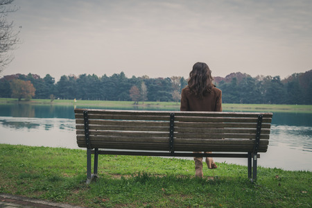 sad lonely: Beautiful young woman with long hair sitting on a bench in a city park