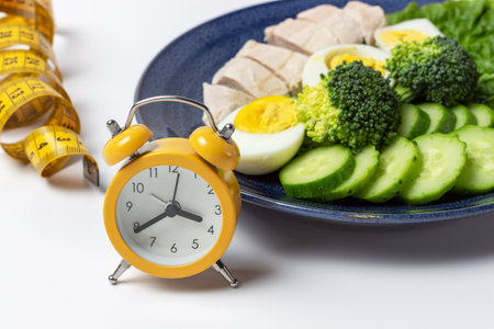 Assiette avec salade, réveil et ruban à mesurer sur fond blanc
