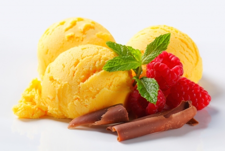 Three scoops of yellow ice cream with raspberries and chocolate curls