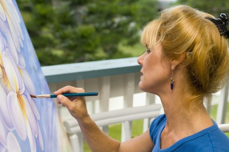 A female artist painting on canvas on her studio balcony Фото со стока