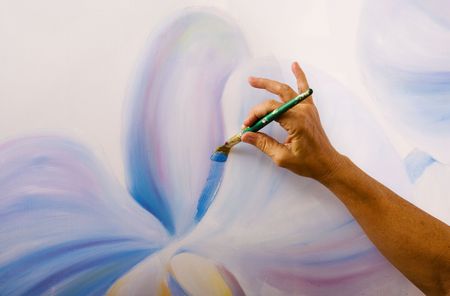 A hand of a female artist painting orchids on canvas in her studio