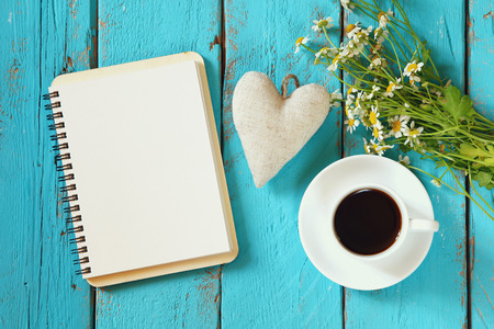 Sun flower: top view image of daisy flowers, blank notebook and fabric heart next to cup of coffee on blue wooden table. Lizenzfreie Bilder