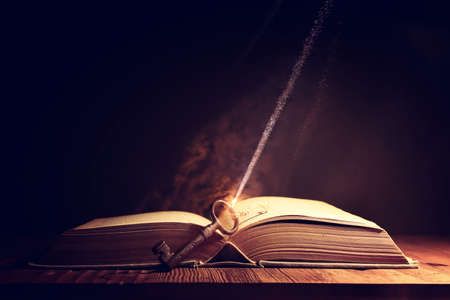 Image of open antique book on wooden table with vintage key
